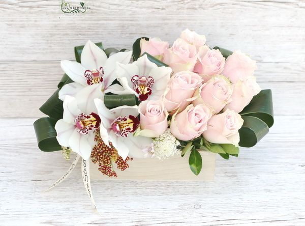 Moderne Komposition mit Orchideen und rosa Rosen in einer Holzkiste