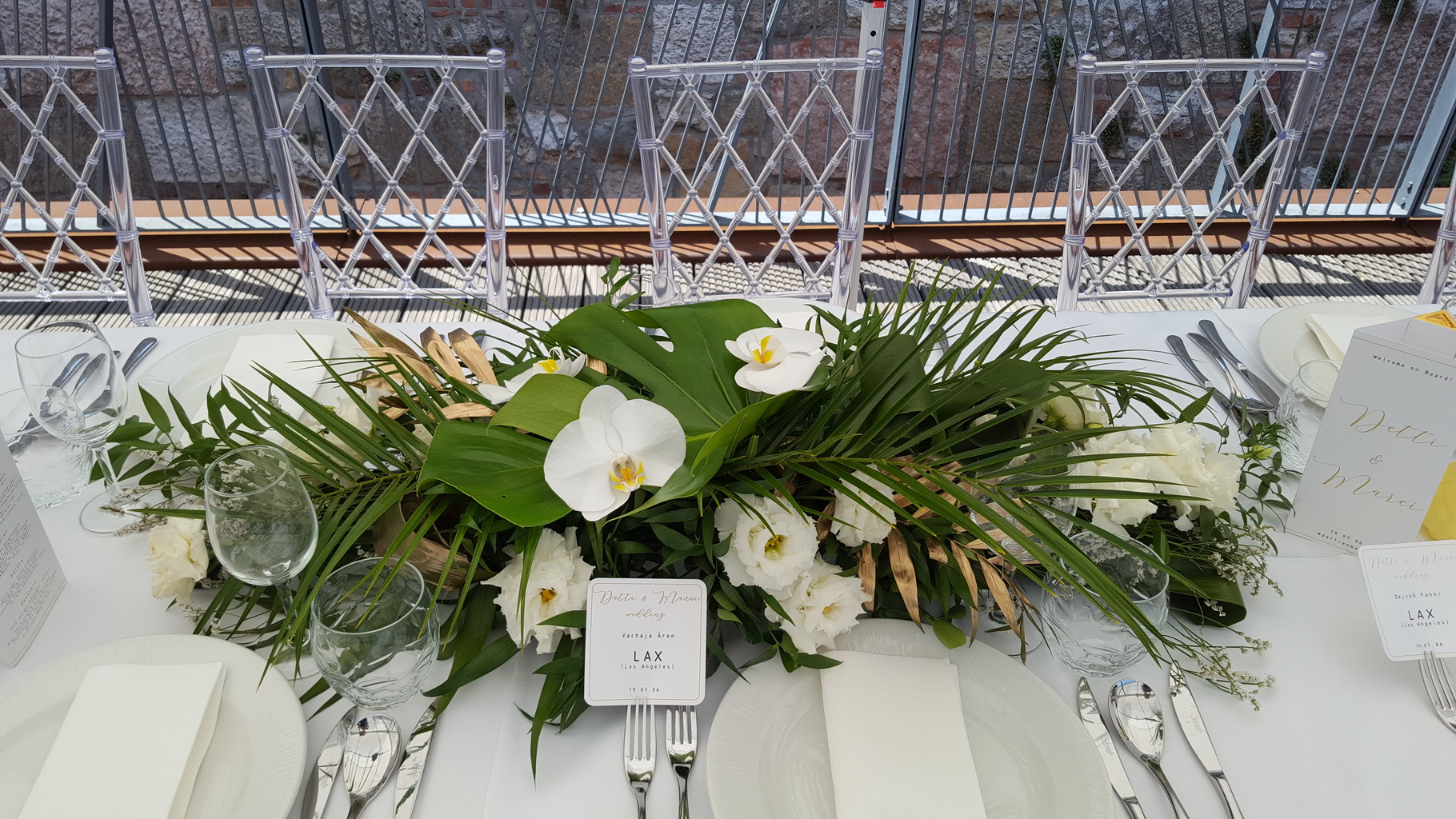 Virágküldés Budapest - Hosszúkás esküvői asztaldísz, Bazaar Eclektica Étterem, Budapest (phalaenopsis orhidea, lizianthus, monstera, pálmalevél, fehér, zöld, arany)